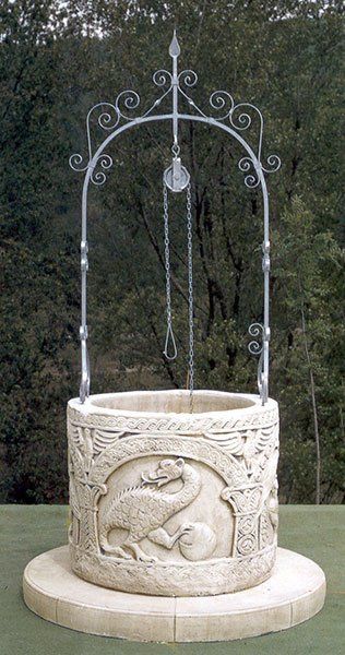 Pozzo in pietra bianca riccamente decorato con arco in ferro battuto, immerso in un giardino.