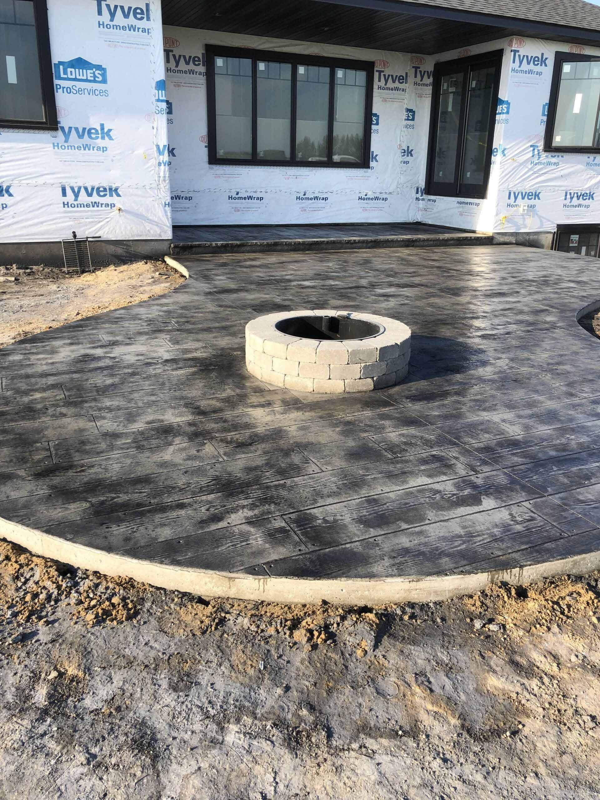 A fire pit is sitting in the middle of a concrete patio in front of a house.