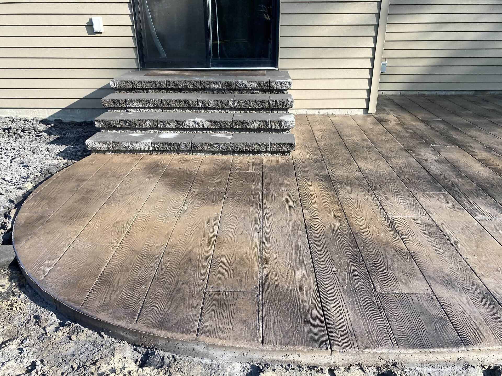 A concrete patio with stairs leading up to the front door of a house.