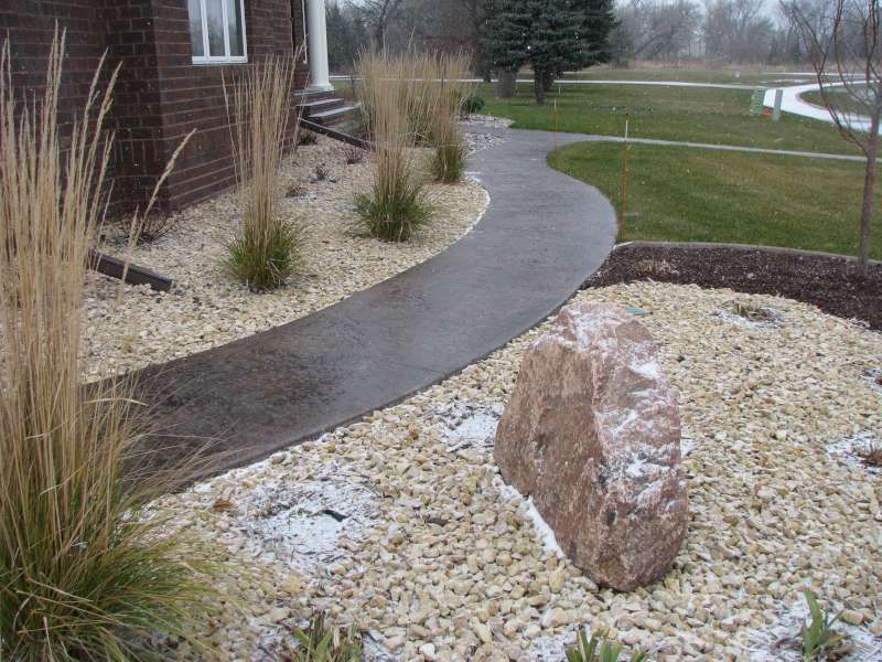 A concrete walkway surrounded by rocks and grass in front of a house.