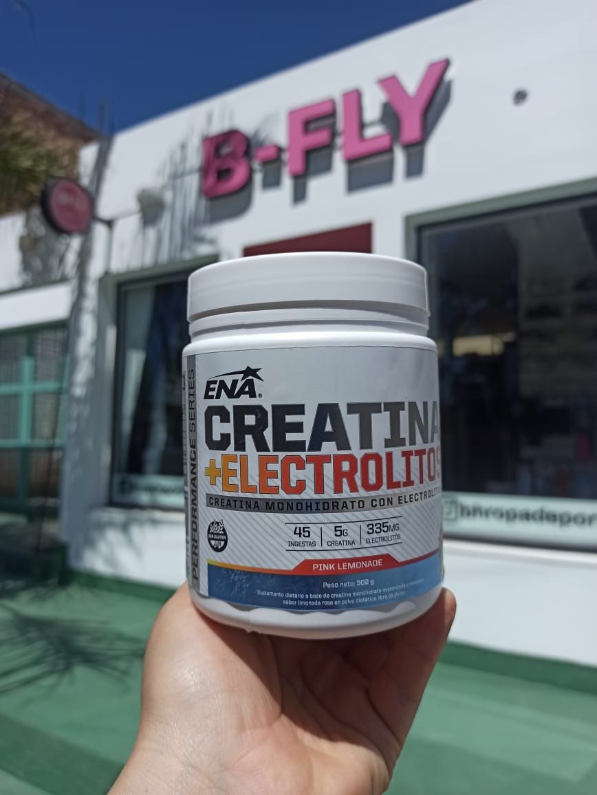 Una mano sostiene un frasco blanco de suplemento de creatina frente a la fachada de una tienda B-FLY.