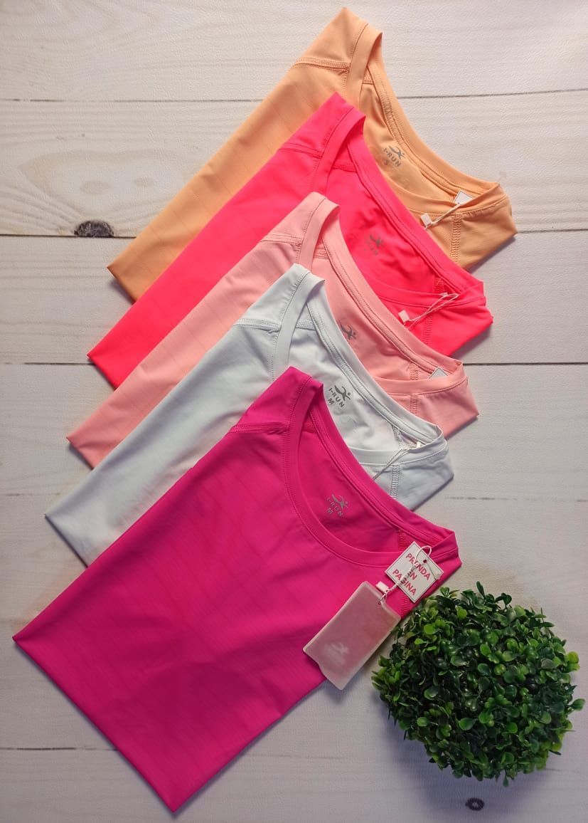 Camisetas de tirantes femeninas dobladas y apiladas en tonos melocotón, coral, gris y rosa junto a una pequeña planta verde.