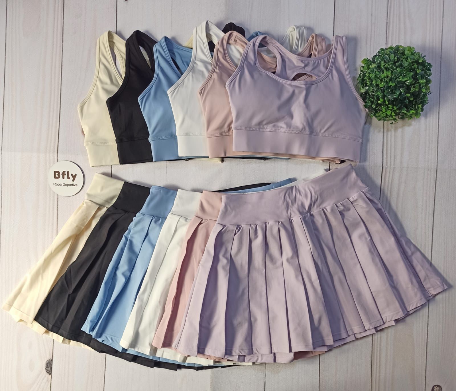 Conjunto deportivo en tonos pastel con tops cortos y faldas plisadas dispuestas sobre un suelo de madera clara.