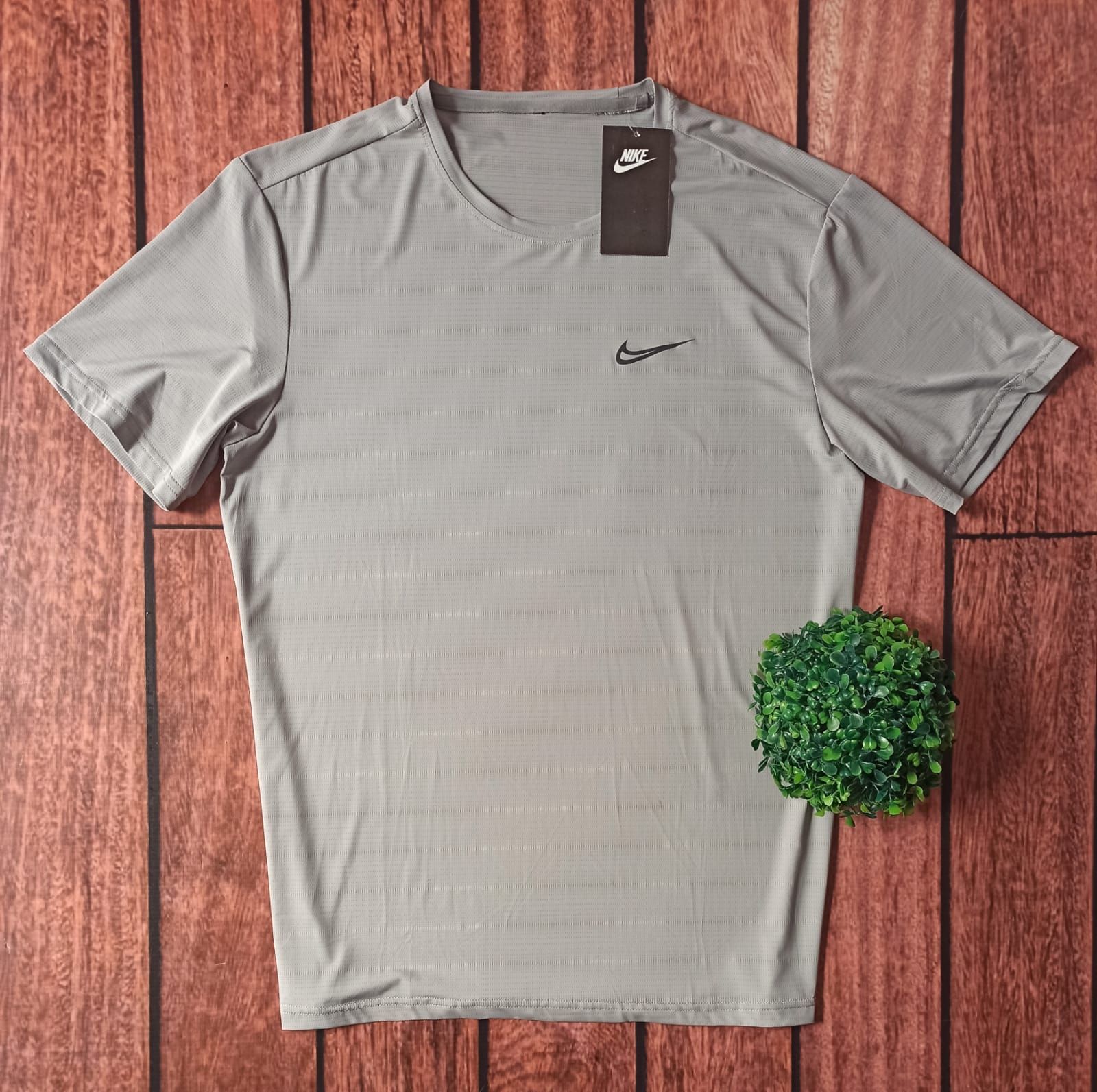 Camiseta deportiva gris de manga corta de Nike sobre una superficie de madera con una pequeña planta verde cerca.