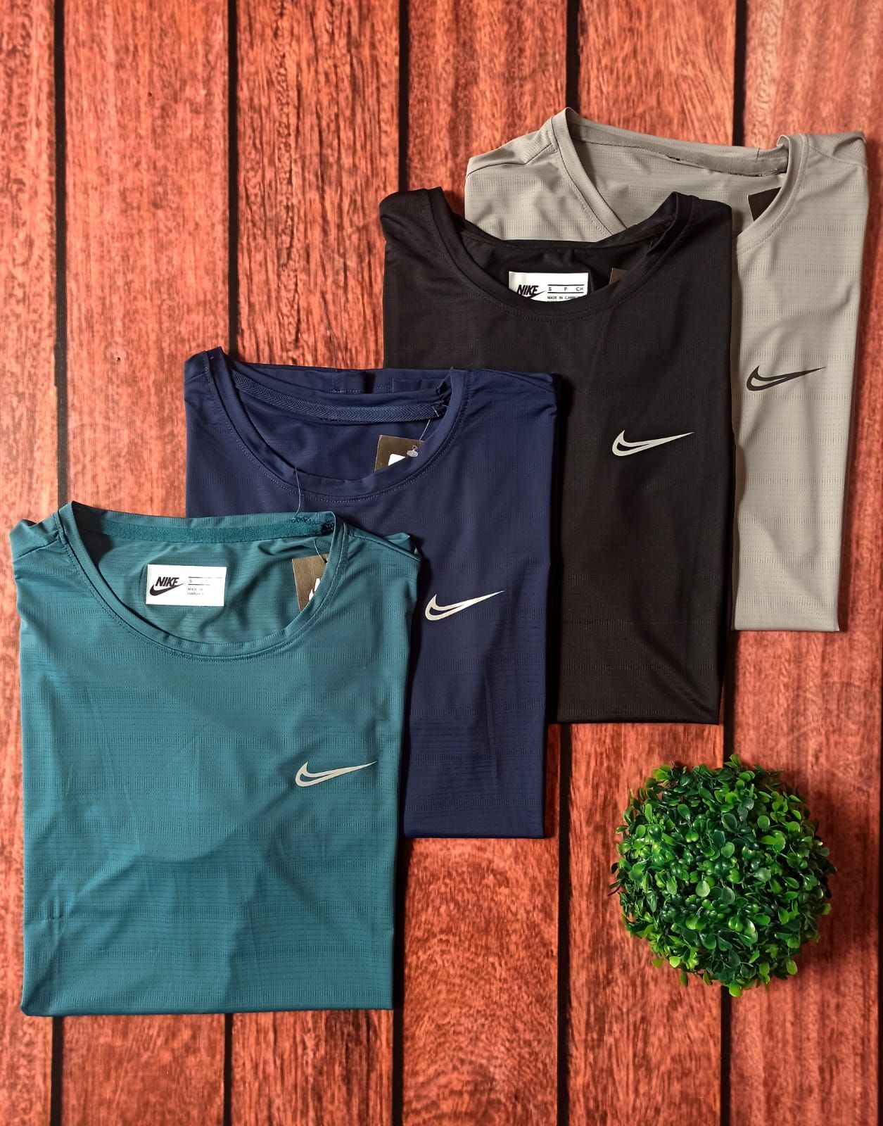 Camiseta deportiva gris de manga corta de Nike sobre una superficie de madera con una pequeña planta verde cerca.