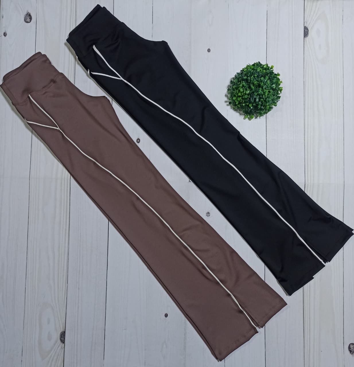 Dos pares de pantalones deportivos, uno negro y otro marrón, yacían en diagonal sobre un suelo de madera clara.