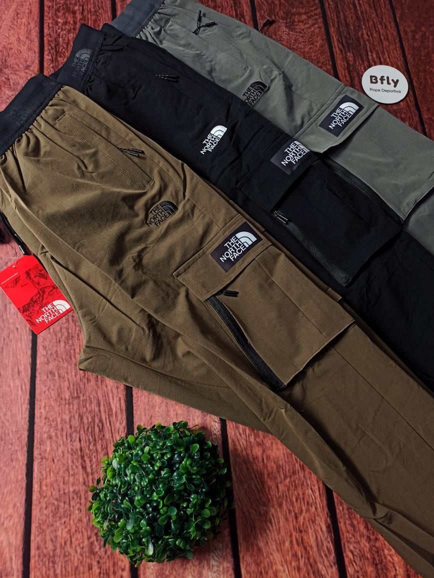 Tres pares de pantalones cargo The North Face en marrón, negro y gris, con parches de logotipo y una pequeña planta.
