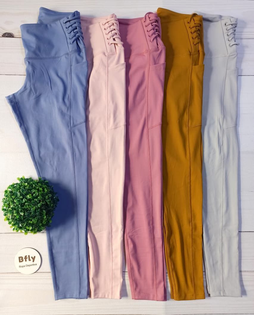 Unos leggings rosas extendidos sobre una superficie de madera blanca junto a una pequeña planta verde.