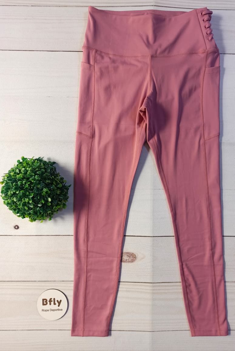 Unos leggings rosas extendidos sobre una superficie de madera blanca junto a una pequeña planta verde.