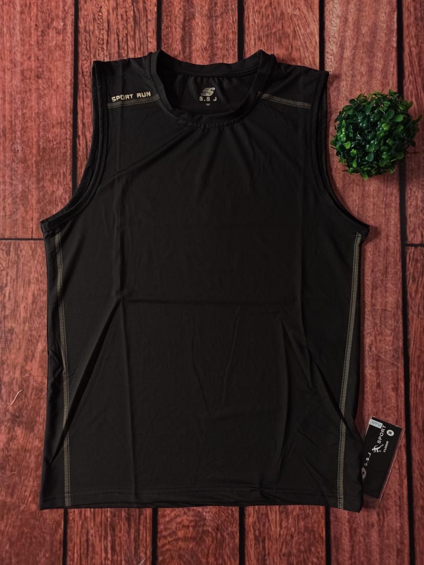 Una camiseta deportiva negra sin mangas extendida sobre una superficie de madera con una pequeña planta verde al lado.