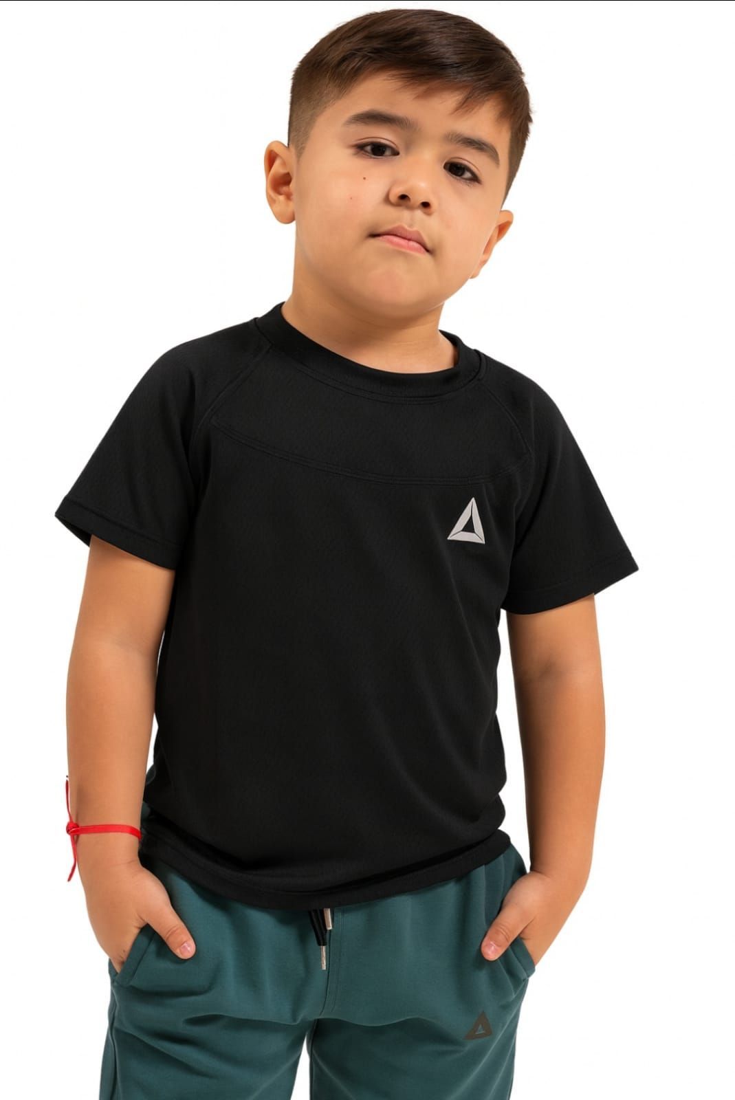 Niño de pie con una camiseta negra y pantalones verdes sobre un fondo blanco.