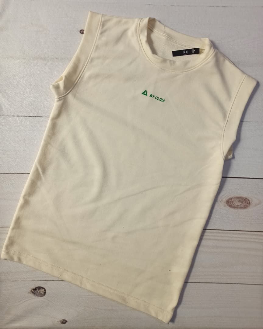 Niña sonriente modelando una camiseta sin mangas color crema y pantalones cortos azules sobre un fondo liso.