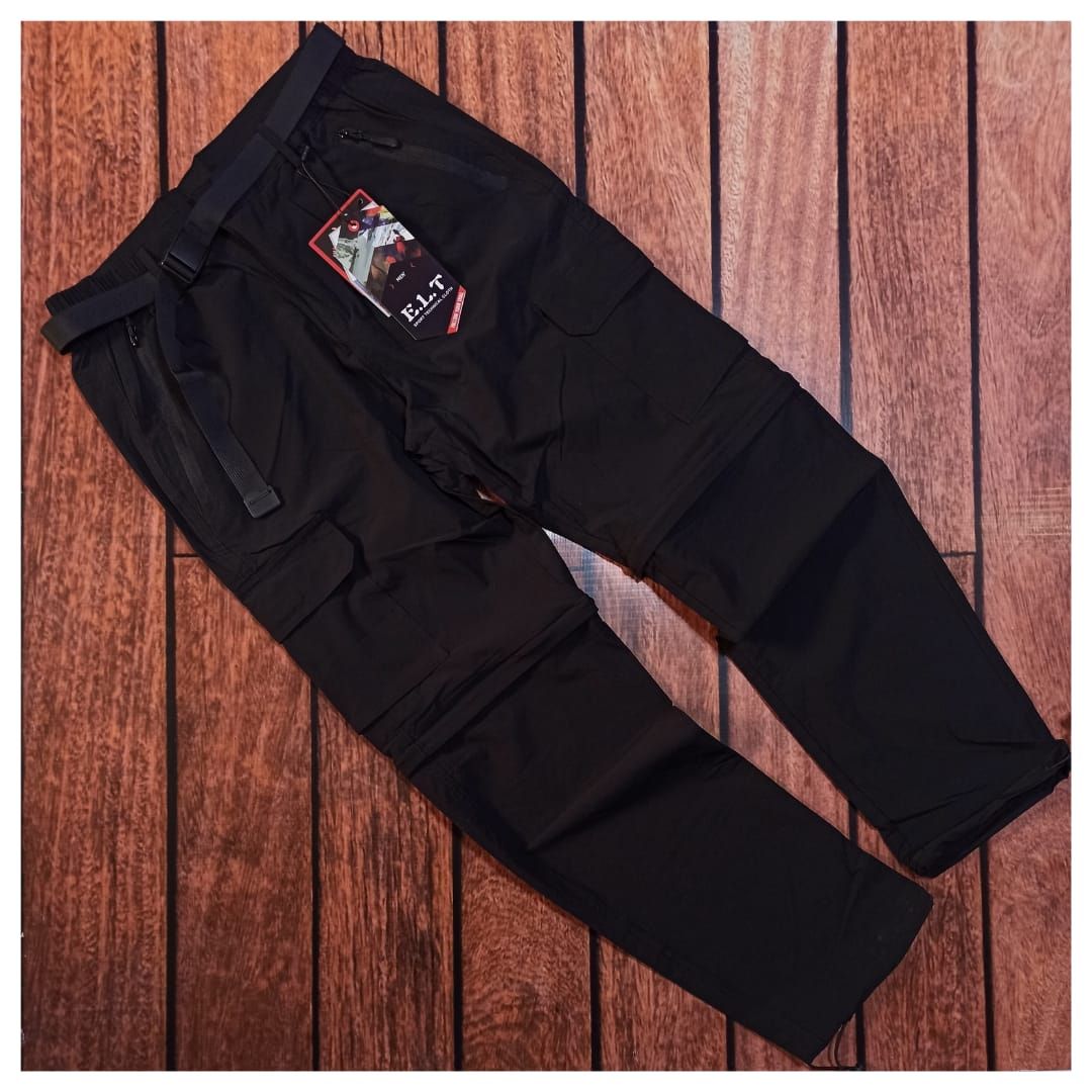 Unos pantalones cargo negros extendidos sobre un suelo de madera, mostrados desde un ángulo.