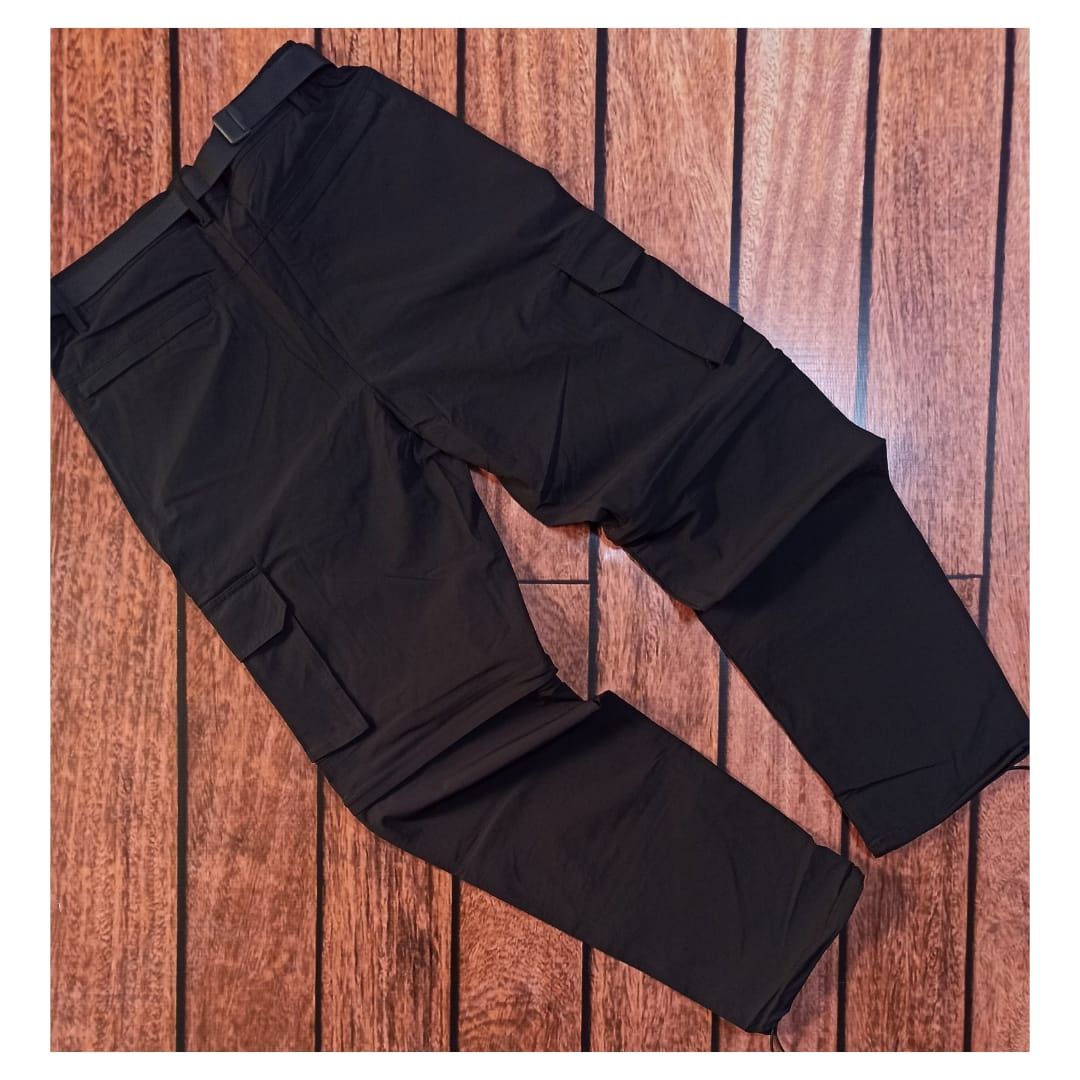 Unos pantalones cargo negros extendidos sobre un suelo de madera, mostrados desde un ángulo.