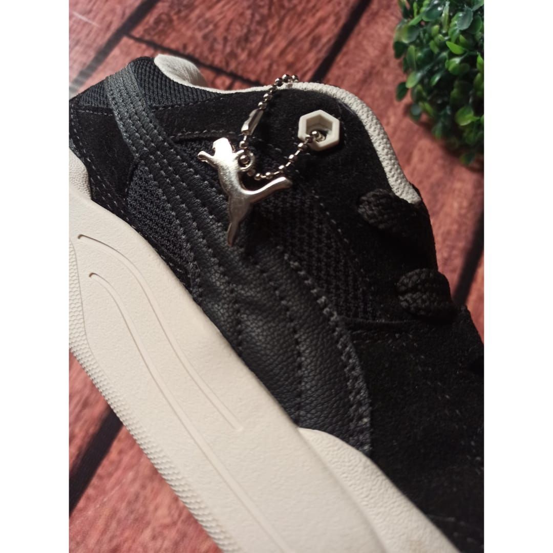 Una zapatilla negra con suela blanca sostenida frente al escaparate de una tienda OKEY.