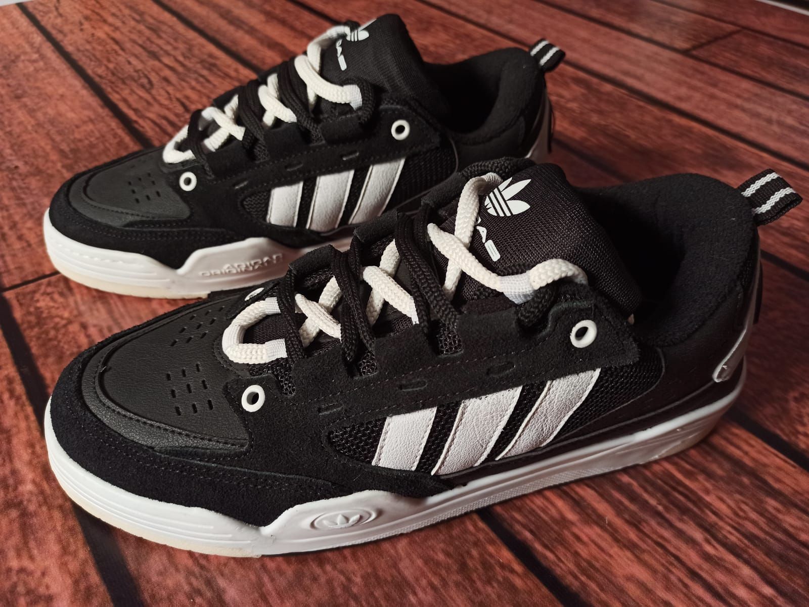 Un par de zapatillas Adidas blancas y negras sobre un suelo de madera.