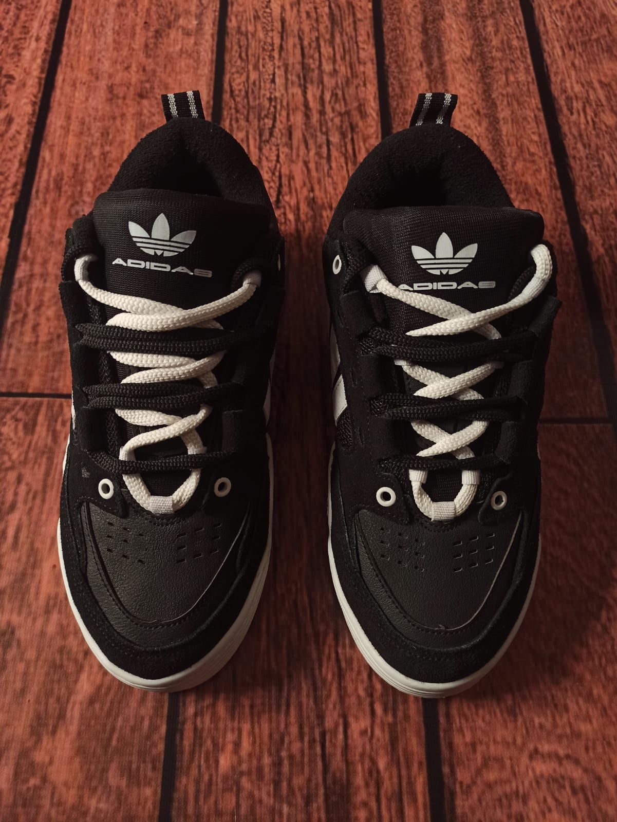 Un par de zapatillas Adidas blancas y negras sobre un suelo de madera.
