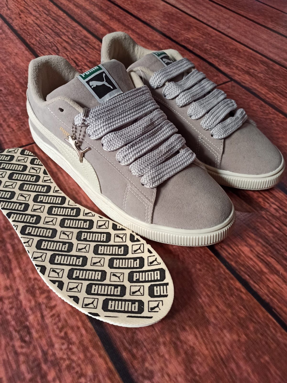 Un par de zapatillas grises con suelas estampadas en blanco y negro sobre un suelo de madera.