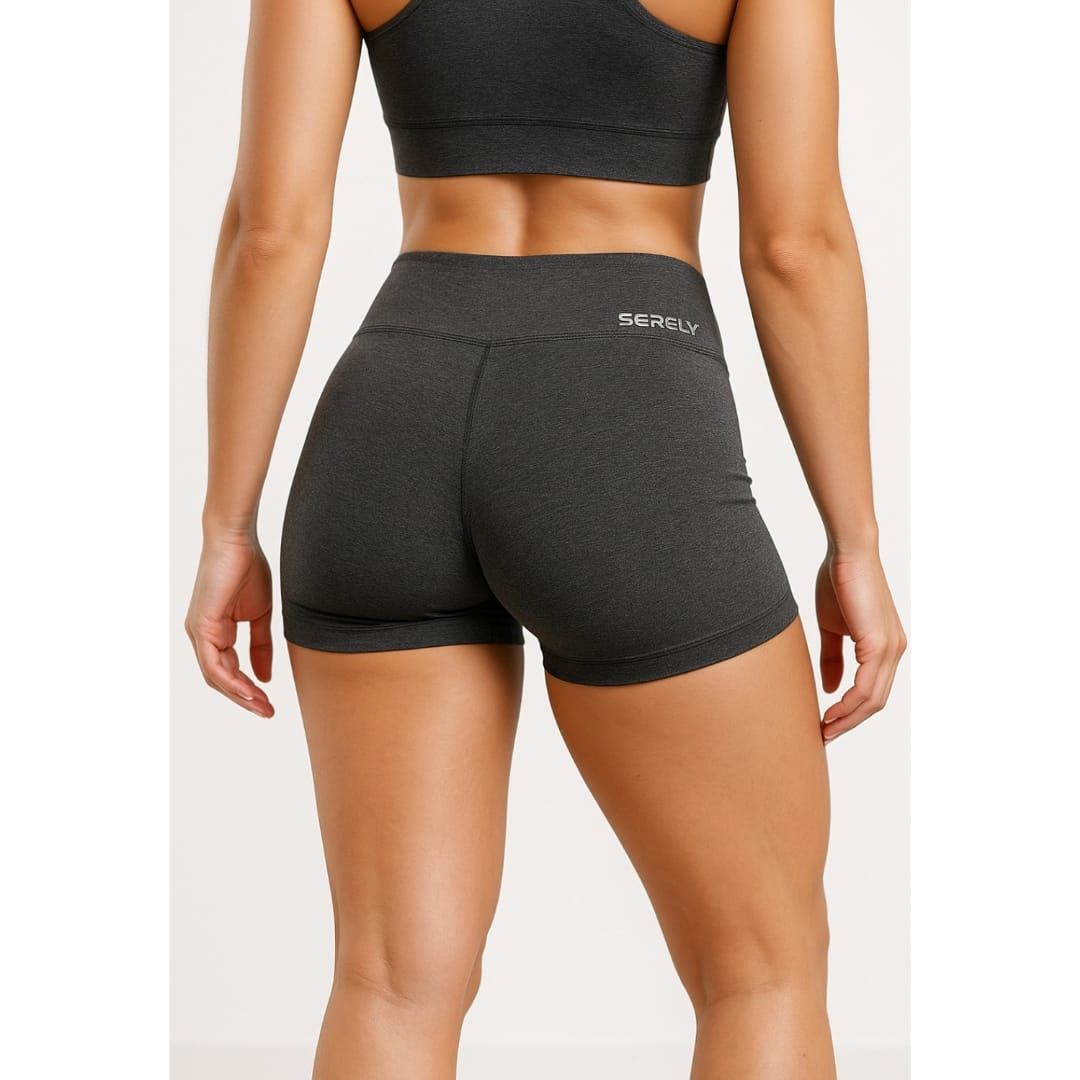 Mujer con sujetador deportivo verde neón y pantalones cortos oscuros de pie frente a un fondo de estudio liso.