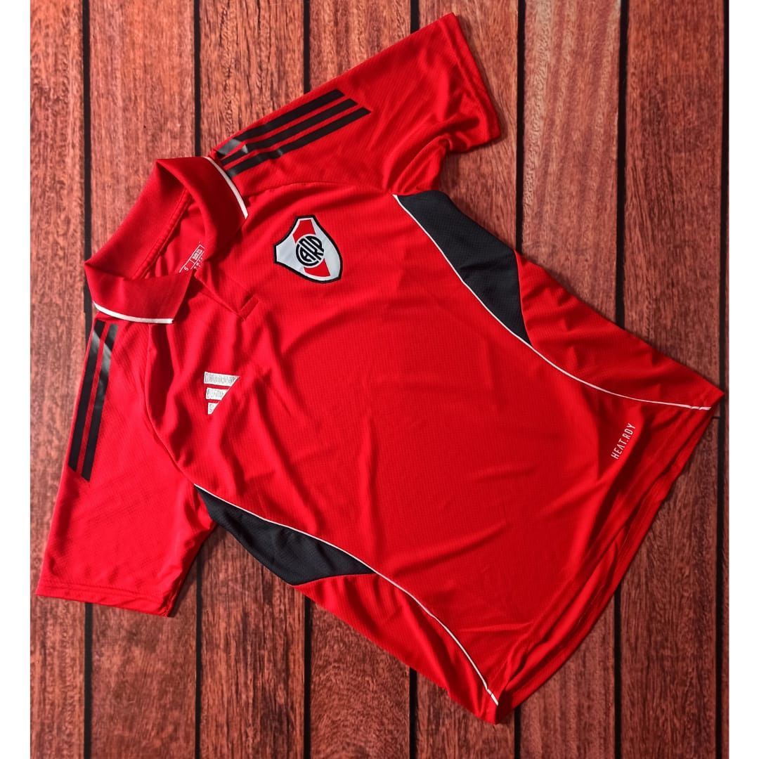 Polo Adidas de rayas rojas con el escudo del equipo en un maniquí masculino sobre un fondo blanco.