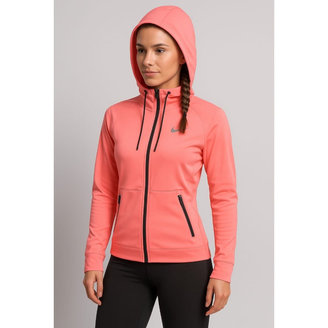 Mujer con chaqueta con capucha y cremallera color coral y pantalones negros sobre un fondo gris liso.