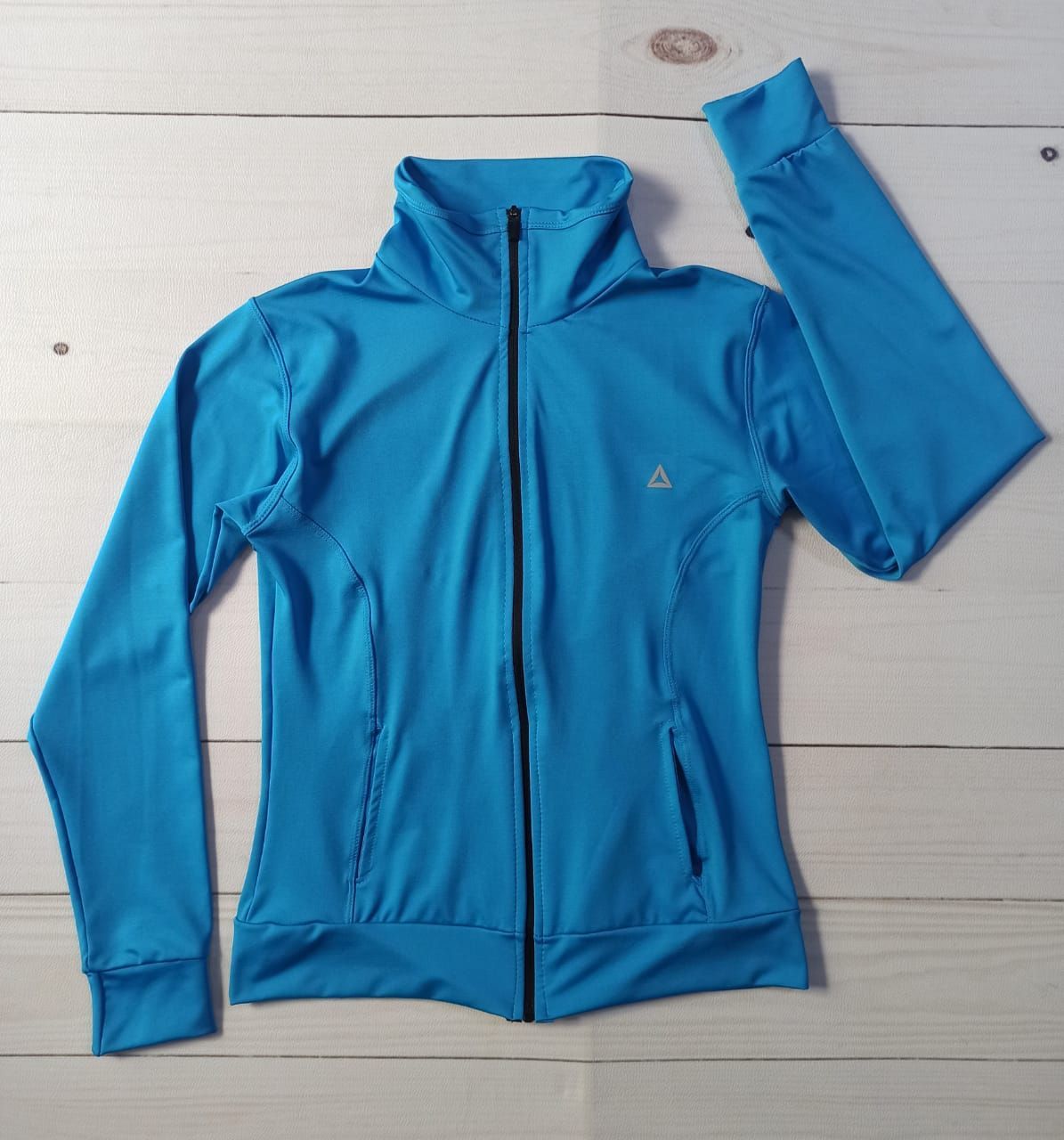 Mujer con una chaqueta deportiva azul con cremallera sobre un fondo blanco.