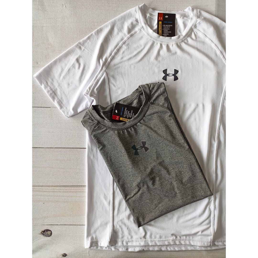 Dos camisetas Under Armour dobladas, una blanca y otra gris, yacían sobre un suelo de baldosas.