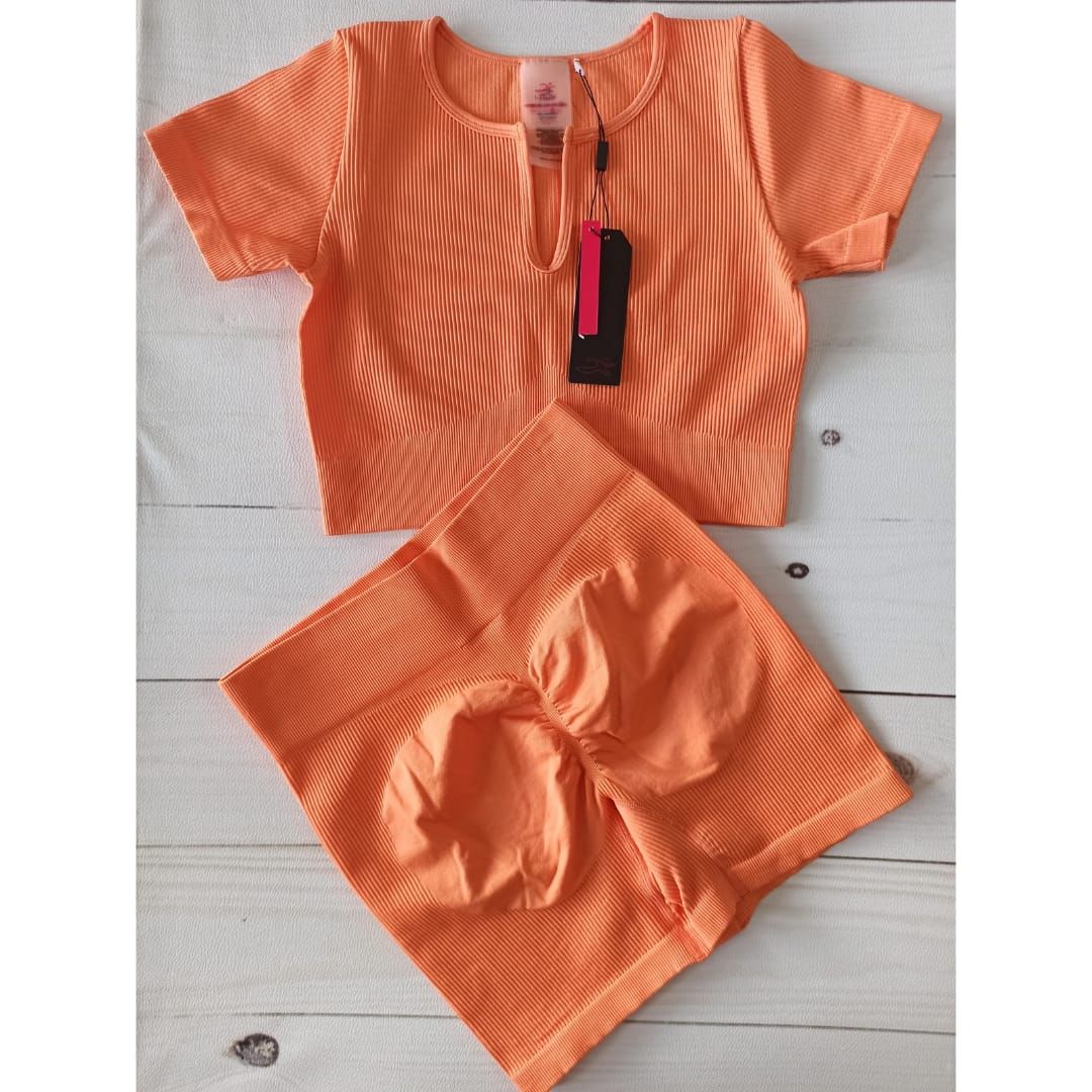 Mujer posando con ropa deportiva naranja sobre un fondo claro liso.