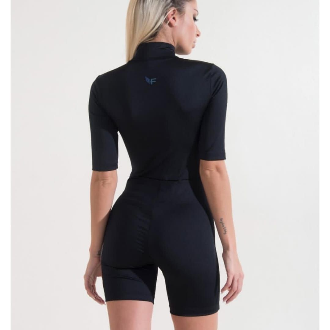 Mujer con vestido deportivo negro con texto de neón en la manga, de perfil lateral sobre un fondo liso.