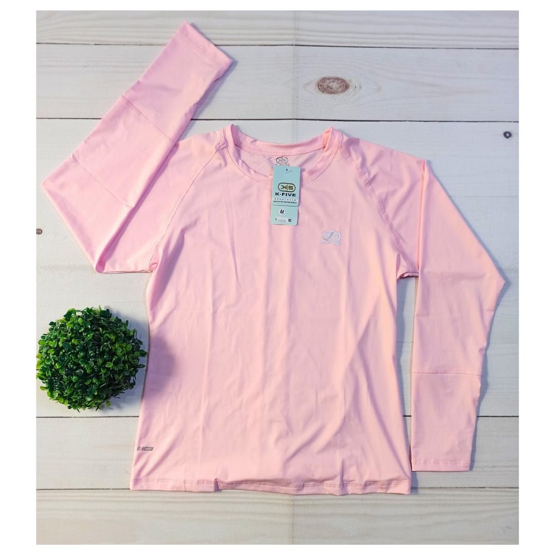Camisa rosa de manga larga extendida sobre un fondo de madera blanca junto a una pequeña planta verde.