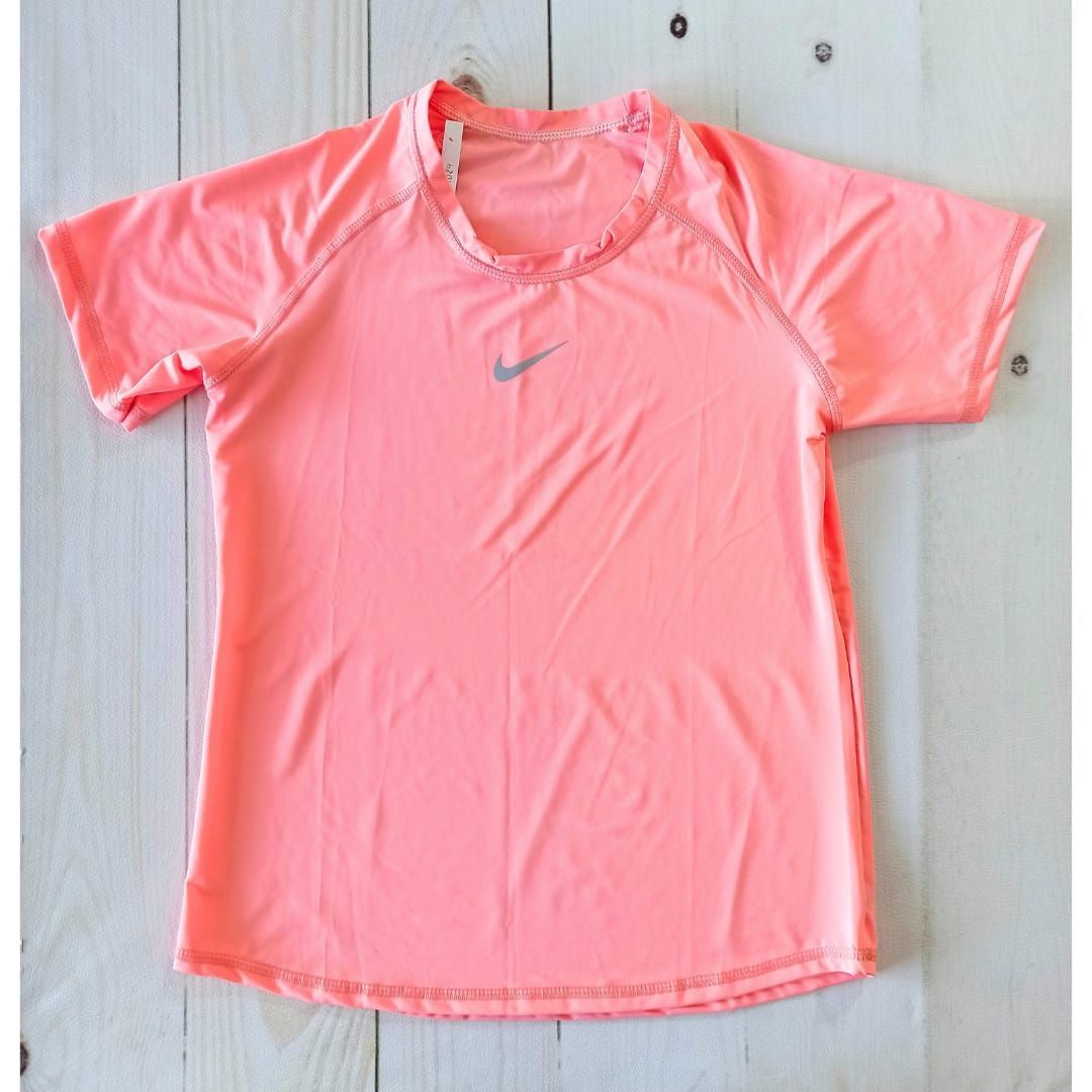 Mujer haciendo ejercicio al aire libre con una camiseta rosa y mallas negras, con vegetación al fondo.