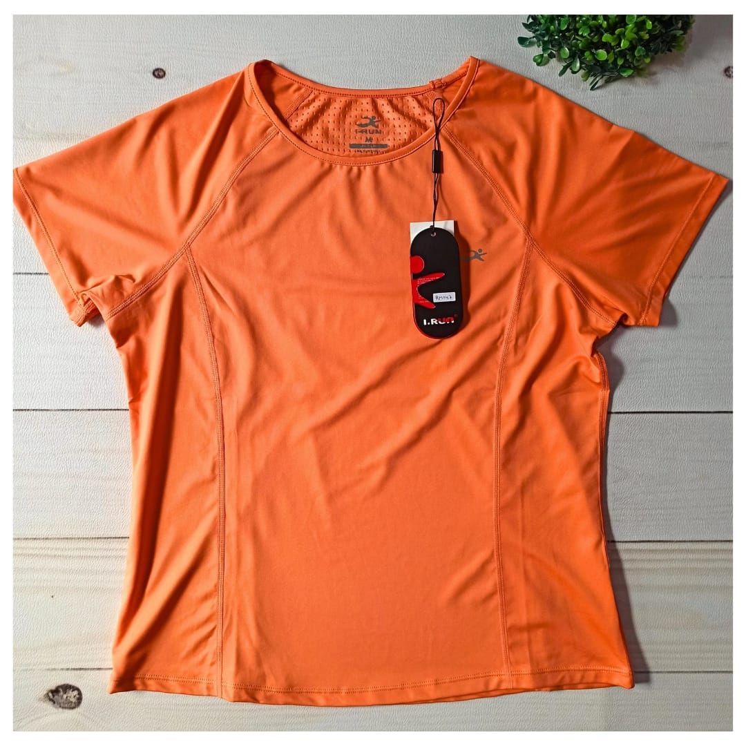 Camiseta naranja de manga corta extendida sobre una superficie de azulejos con la etiqueta colgando.