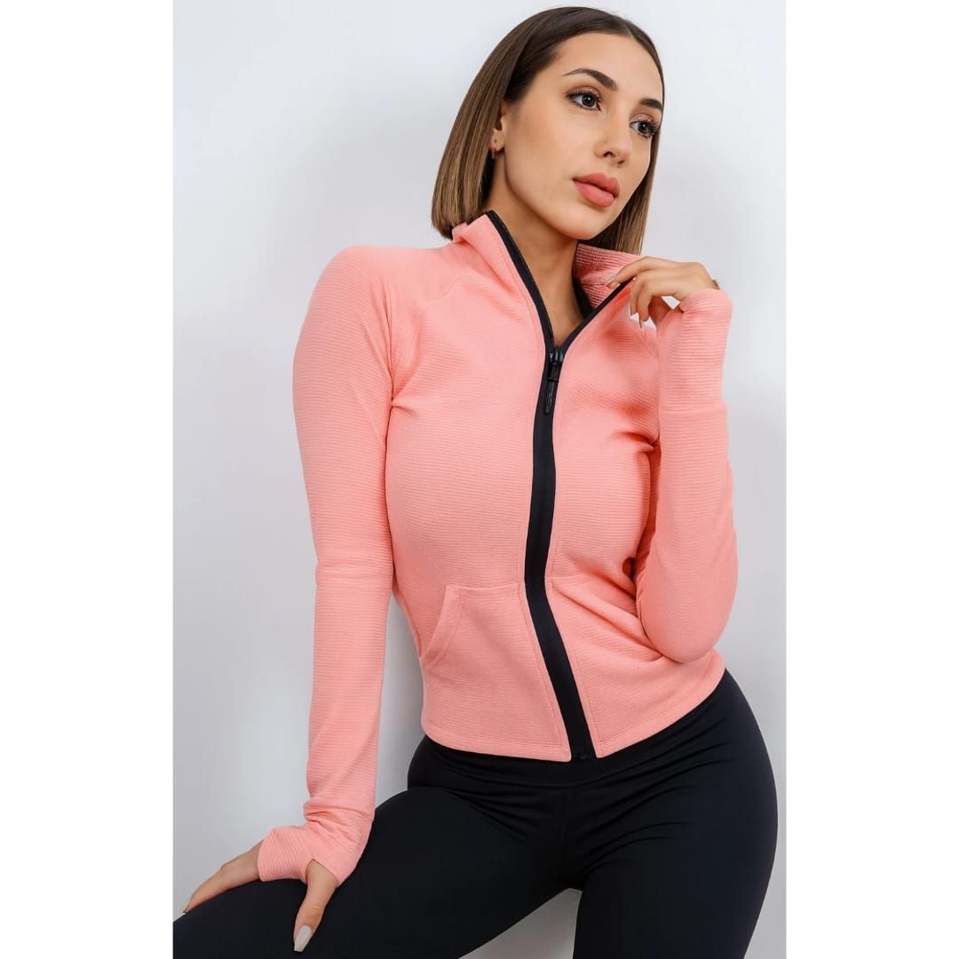 Mujer con top rosa con cremallera y pantalones negros posando sobre un fondo gris claro.