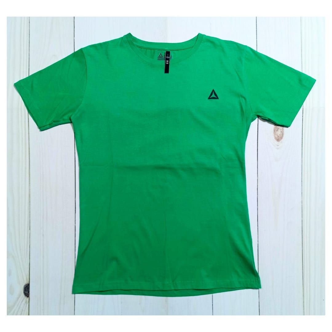 Hombre de pie en un gimnasio sosteniendo mancuernas, vistiendo una camisa verde y pantalones cortos negros.