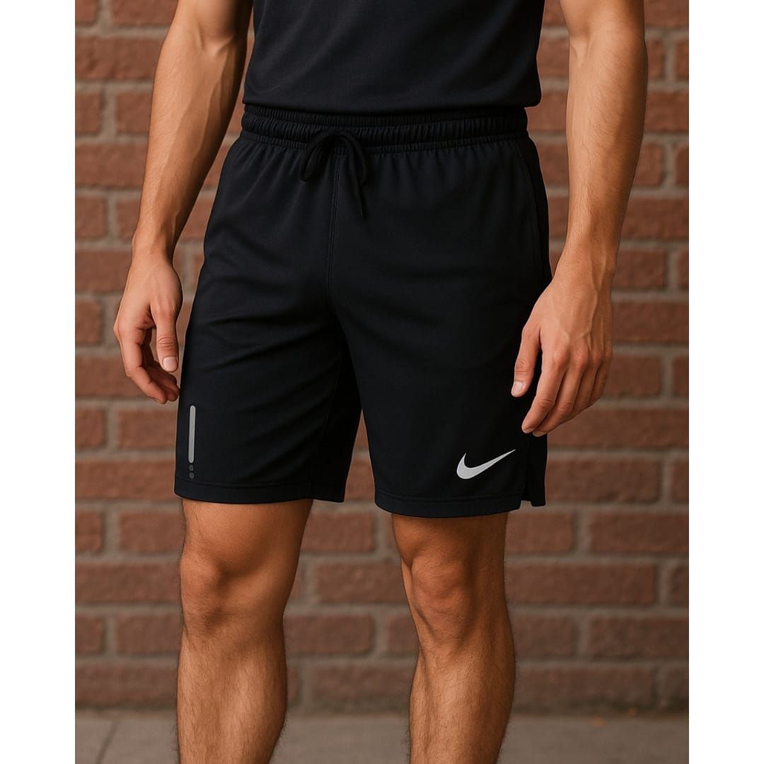 Hombre con pantalones cortos deportivos negros y camiseta sin mangas de pie contra una pared de ladrillos.