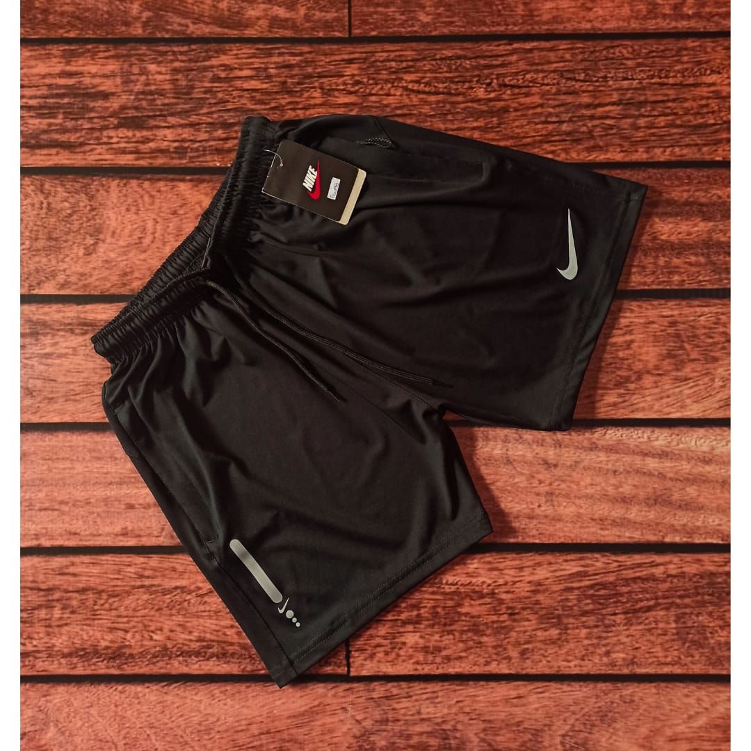 Hombre con pantalones cortos deportivos negros y camiseta sin mangas de pie contra una pared de ladrillos.
