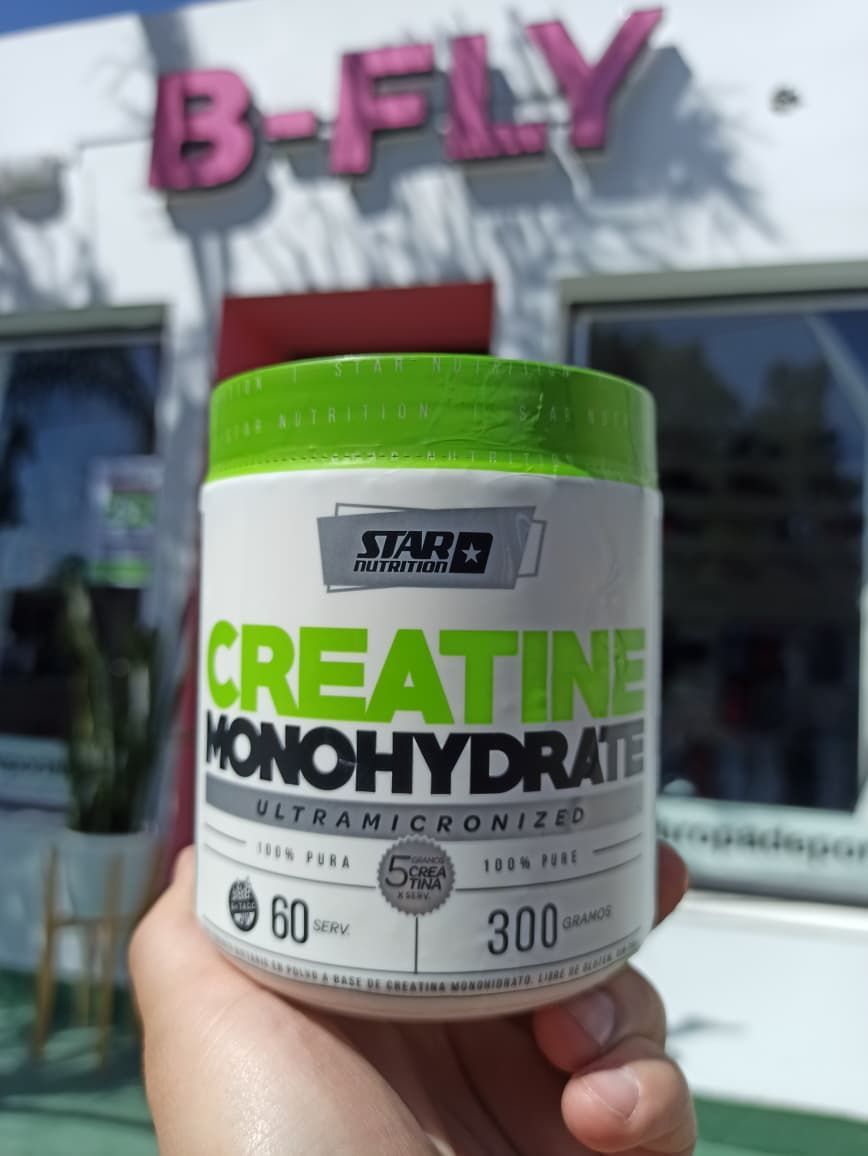 Frasco de monohidrato de creatina con tapa verde frente a una tienda B-Fly.