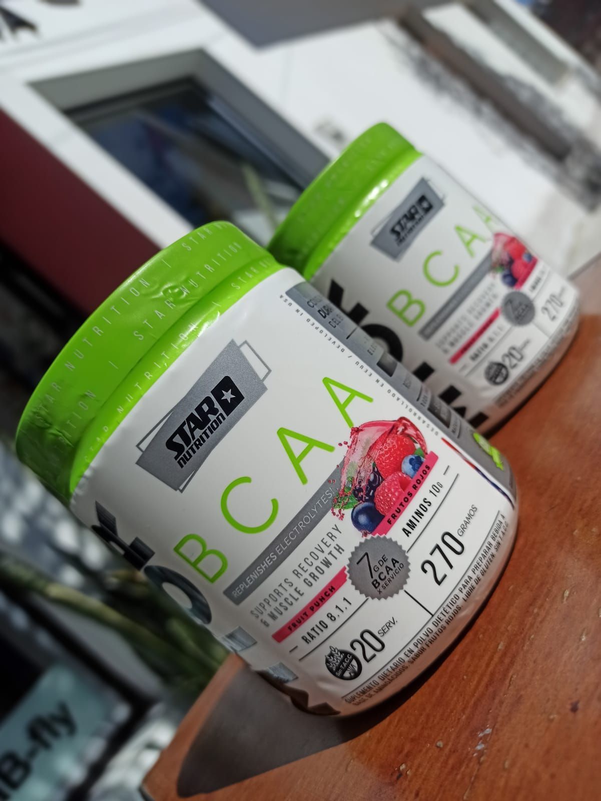 Dos botes de suplementos de BCAA con tapas verdes sobre una mesa de madera, uno de ellos en primer plano.