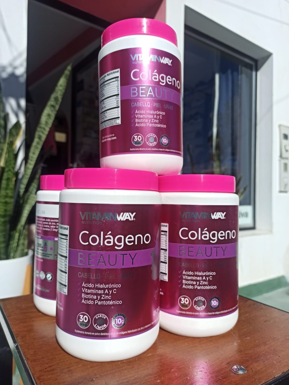 Envases de suplemento Pink Colágeno apilados sobre una mesa al aire libre.