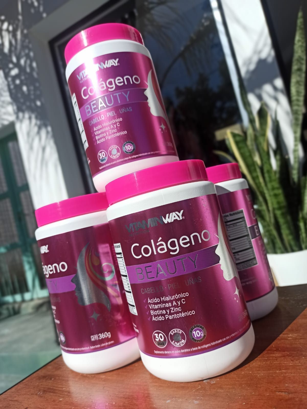 Envases de suplemento Pink Colágeno apilados sobre una mesa al aire libre.