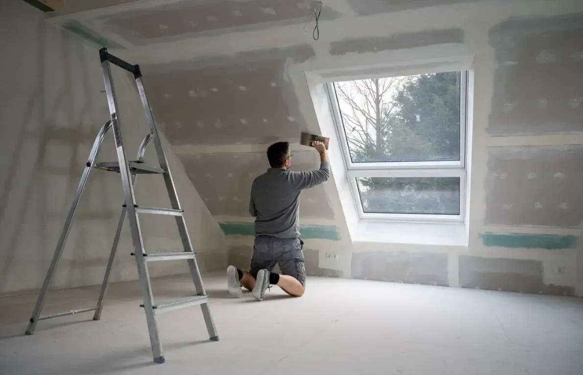 Man applying plaster to attic drywall near window.