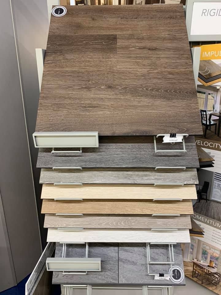Display of wood and tile flooring samples in a showroom, with a brown sample panel on top.