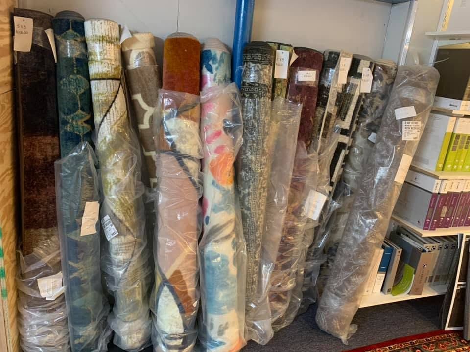 Rolls of patterned rugs and carpet samples stacked upright on shelves in a store or warehouse