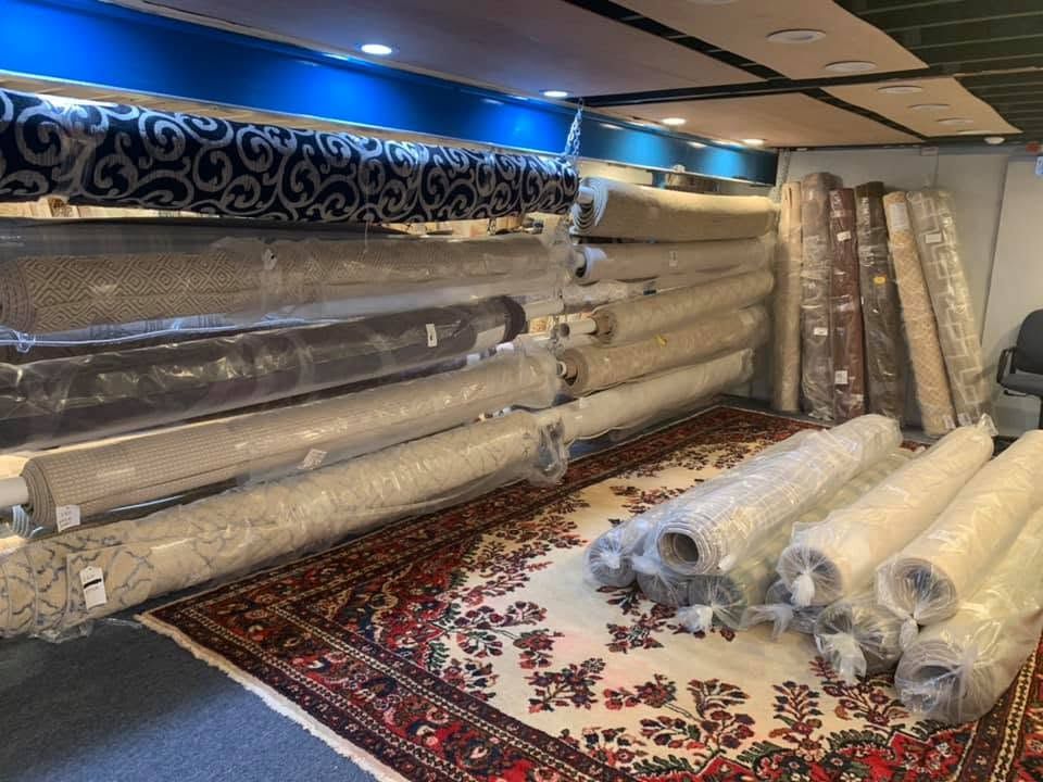 Rolled carpets and rugs stacked in a shop showroom with patterned carpet flooring and wall displays