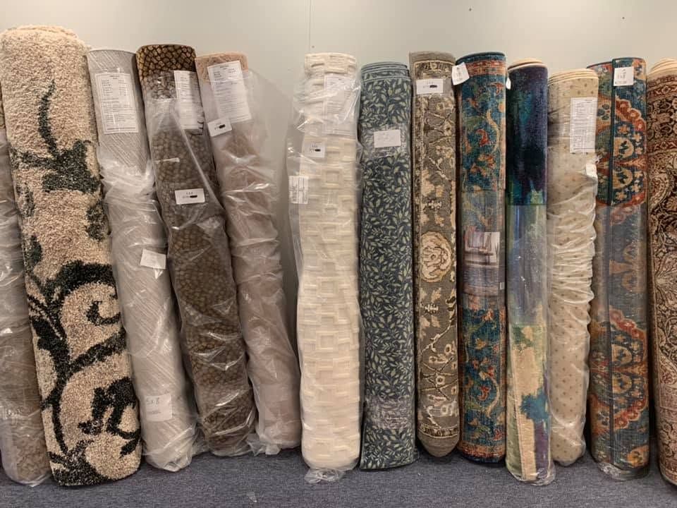 Rolled carpets in various patterns and colors stacked upright on a shelf