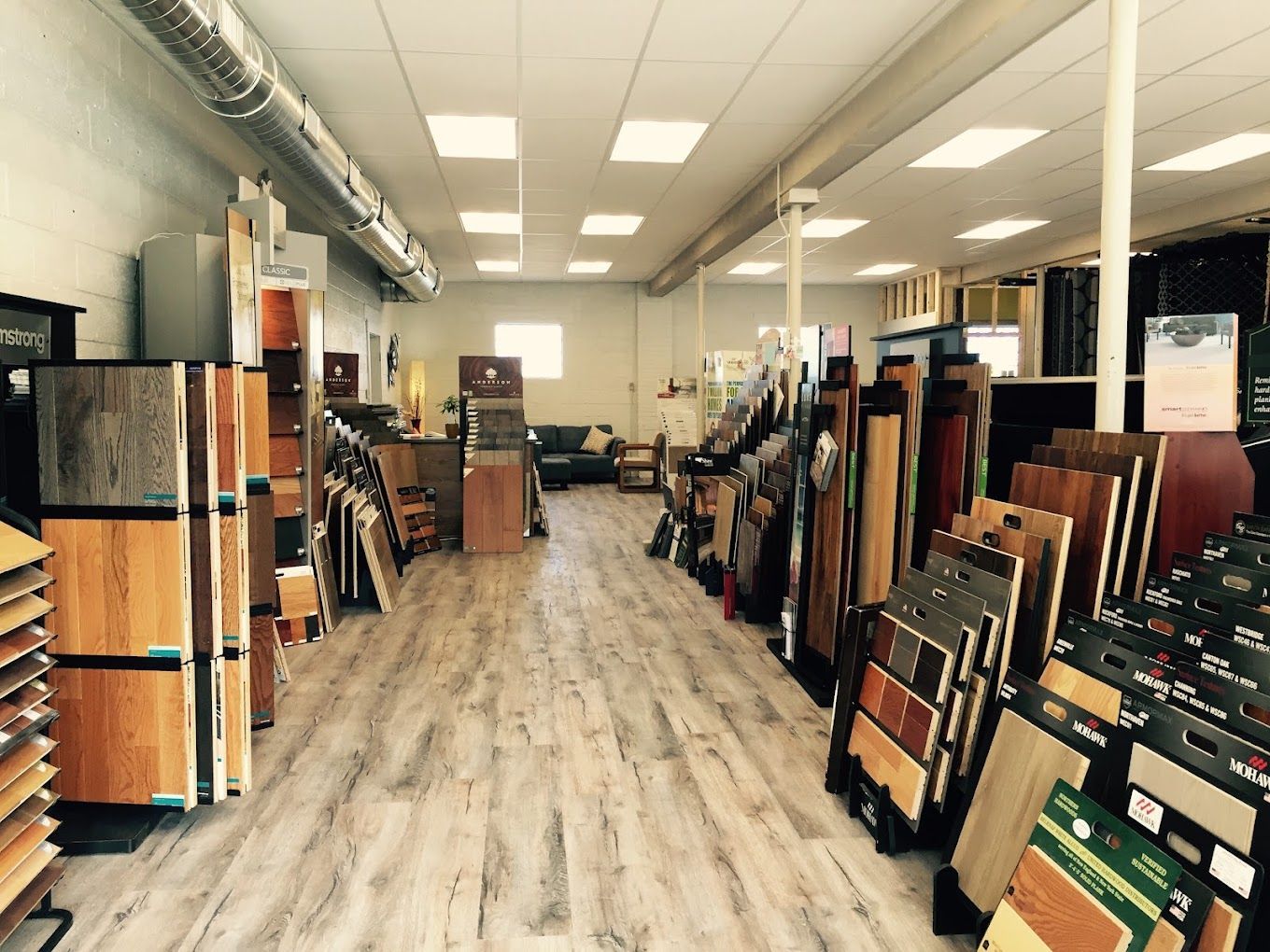 A showroom aisle lined with rugs and flooring samples under bright ceiling lights.