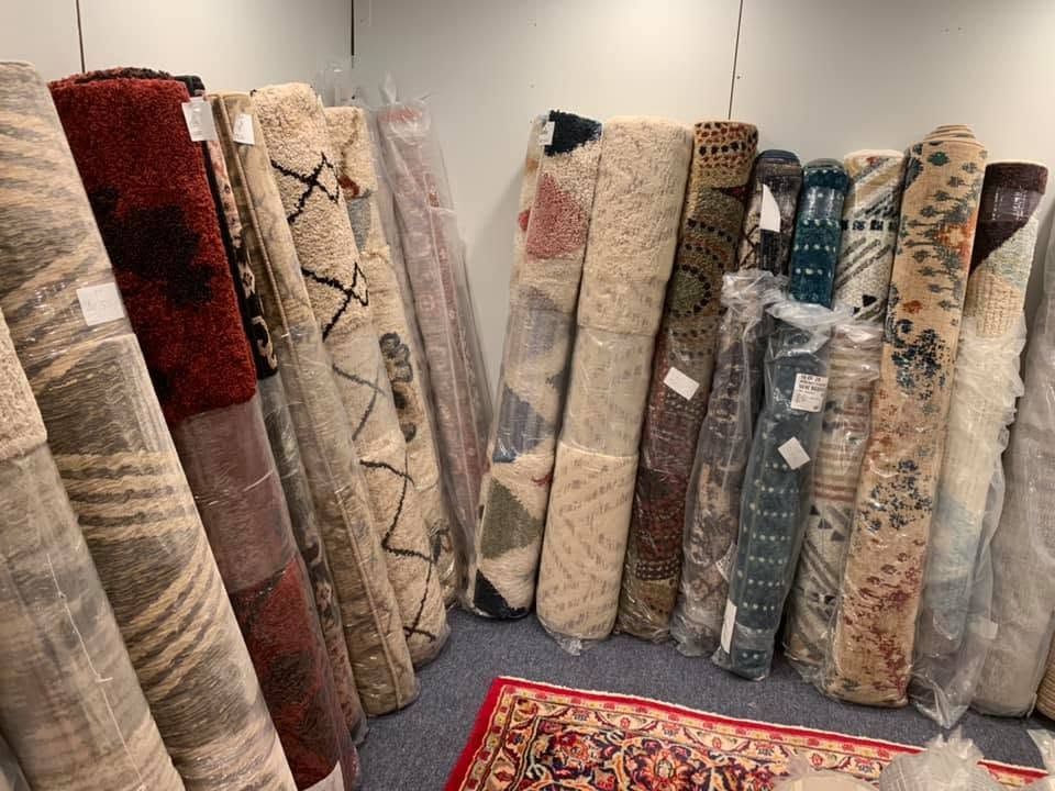 Rolled area rugs displayed upright in a showroom, in varied neutral and patterned designs.