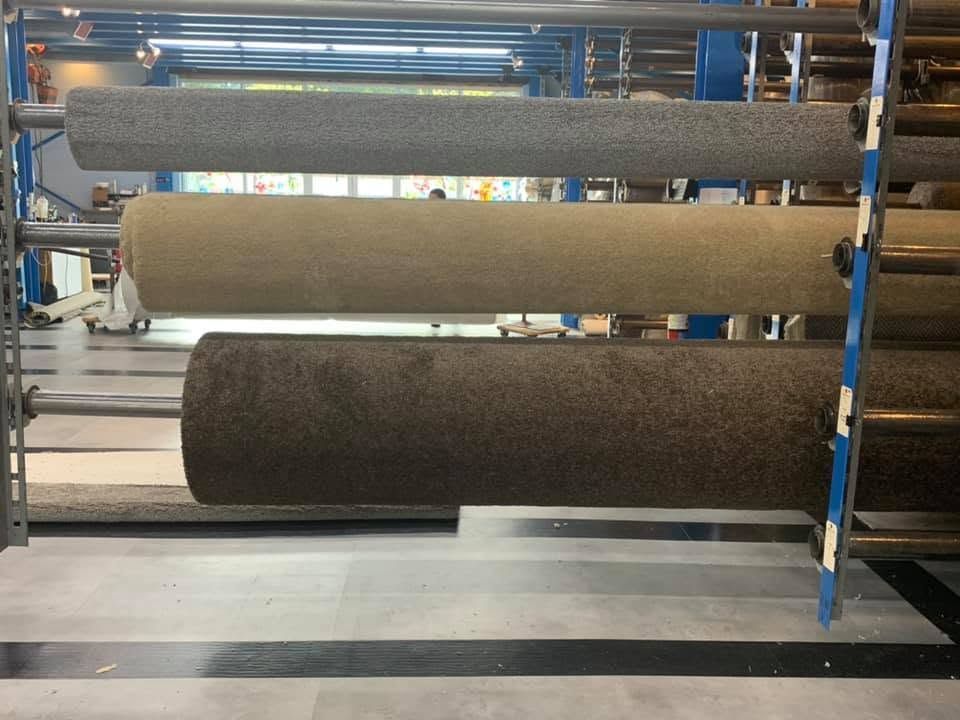 Large rolls of carpet or fabric stored on industrial shelving in a warehouse.