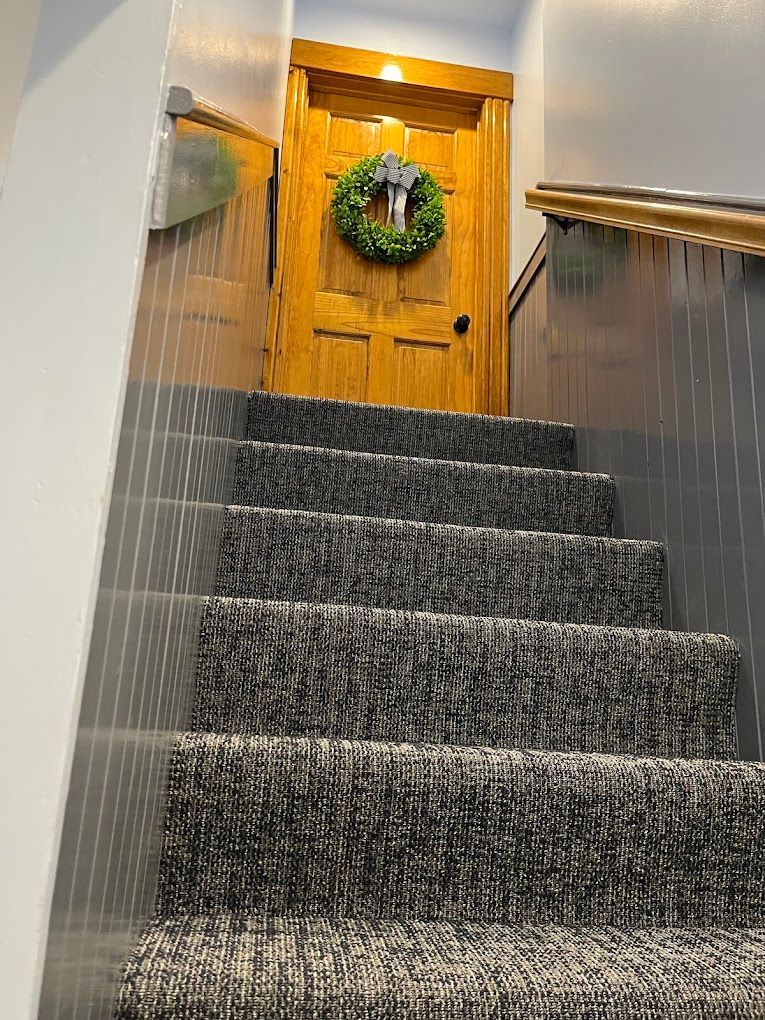 Carpeted staircase leading to a wooden door with a green wreath at the top.