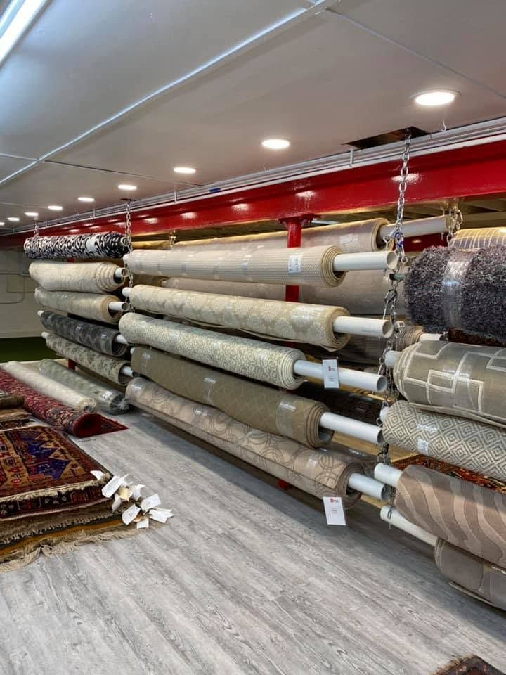 Carpet showroom with stacked rolled rugs on white shelves under bright ceiling lights